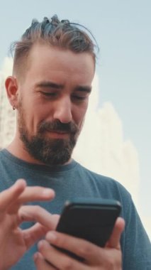 VERTICAL VIDEO: Young man with beard uses map application on mobile phone