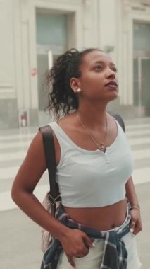 VERTICAL VIDEO: Young mixed race woman stands at the railway station, looks at the information board