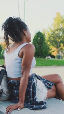 VERTICAL VIDEO: Young mixed race woman sitting on park bench