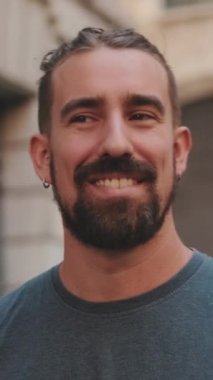 VERTICAL VIDEO: Close-up of Young smiling man with beard walking and looking around