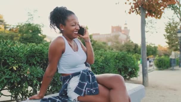 Сміється Молода Змішана Жінка Сидить Лавці Парку Розмовляючи Мобільному Телефоні — стокове відео