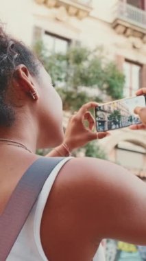 VERTICAL VIDEO: Young mixed race woman uses cell phone, takes photo of the old city