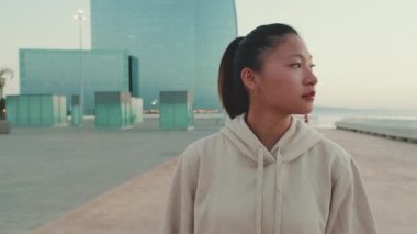 Asian girl wearing sportswear walks outside, looks around at morning time