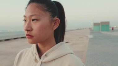 Close-up of an Asian girl wearing sportswear turns her head and looks at the camera at morning time