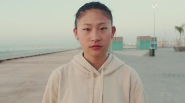 Close-up of an Asian girl wearing sportswear walking and looking at the camera at morning time