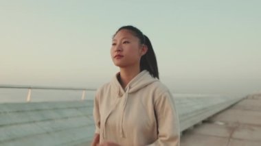 Asian young athletic woman running along the promenade. Sportswoman in sportswear exercising outdoors at morning time