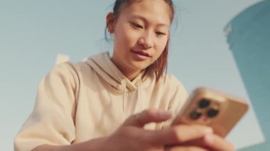 Close up, asian girl in sportswear, rests after training , uses smartphone at sunrise