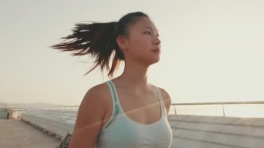 Asian girl in sports top runs along the promenade at morning time
