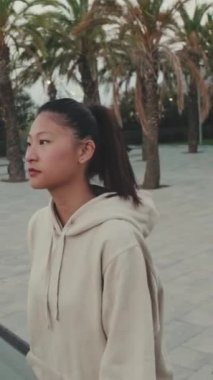 VERTICAL VIDEO: Asian girl wears sportswear, climbs the stairs at morning time on the embankment background