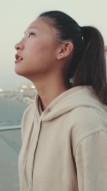 VERTICAL VIDEO: Asian girl wears sportswear, climbs stairs, looks up at morning time