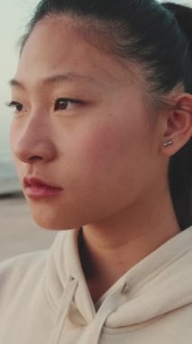 VERTICAL VIDEO: Close-up of an Asian girl wearing sportswear turns her head and looks at the camera at morning time