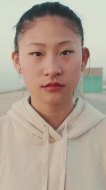 VERTICAL VIDEO: Asian girl wearing sportswear looking at camera at morning time. Camera moving forwards