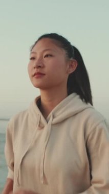 VERTICAL VIDEO: Asian young athletic woman running along the promenade. Sportswoman in sportswear exercising outdoors at morning time