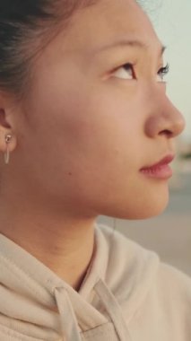 VERTICAL VIDEO: Close up, asian girl in sportswear stands at morning time on modern buildings background