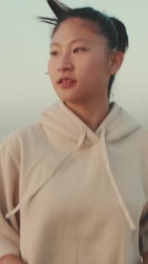 VERTICAL VIDEO: Asian young athletic woman running along the promenade. Sportswoman in sportswear exercising outdoors at morning time