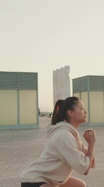 VERTICAL VIDEO: Asian girl in sportswear doing workout, squats, quadriceps exercises at morning time