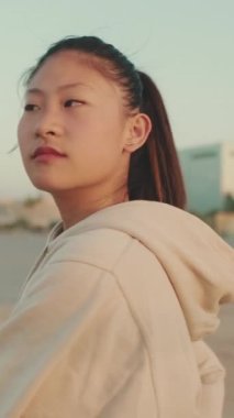 VERTICAL VIDEO: Asian girl in sportswear doing workout, stretching at morning time on modern buildings background