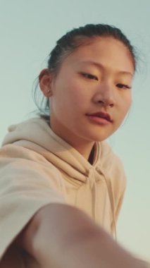 VERTICAL VIDEO: Asian girl in sportswear doing workout, stretching at morning time on modern buildings background