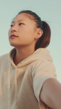 VERTICAL VIDEO: Asian girl in sportswear doing workout, stretching at morning time on modern buildings background