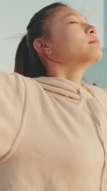 VERTICAL VIDEO: Asian girl in sportswear doing workout, breathing exercises, relaxing at morning time
