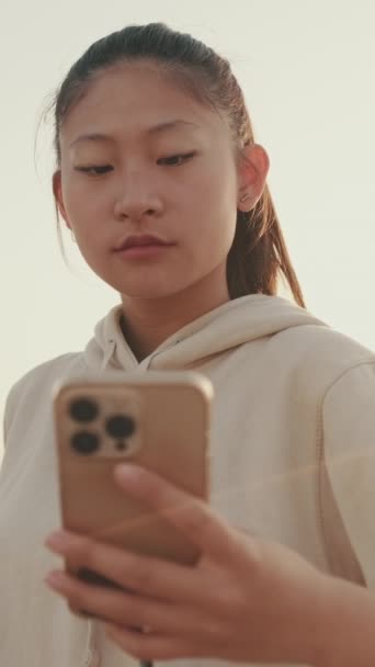 Vertical Video Asian Girl Sportswear Uses Phone While Standing Waterfront — Stok video