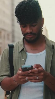 VERTICAL VIDEO: Young smiling man with beard dressed in an olive-colored shirt uses phone