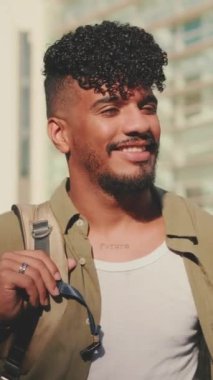 VERTICAL VIDEO: Young male student dressed in an olive colored shirt turns his head and smiles at the camera from outside next to the university
