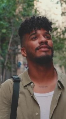 VERTICAL VIDEO: Close up, young smiling man dressed in an olive-colored shirt walks along the narrow street of the old city and looks around