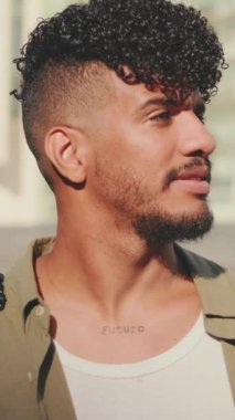 VERTICAL VIDEO: Close up, young male student dressed in an olive colored shirt turns his head and smiles at the camera from outside next to the university