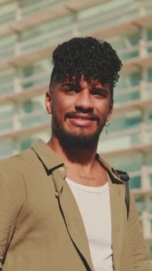 VERTICAL VIDEO: Young male student dressed in an olive-colored shirt walks from outside next to the university