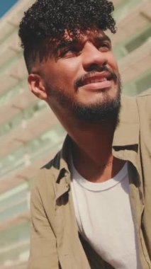 VERTICAL VIDEO: Close up, young male student dressed in an olive colored shirt sits outside next to university