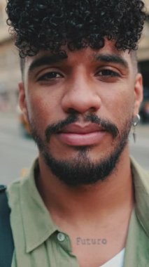 Yakından, zeytin rengi gömlek giymiş sakallı mutlu genç adam yolun kenarında duruyor, gülümsüyor ve kameraya bakıyor.