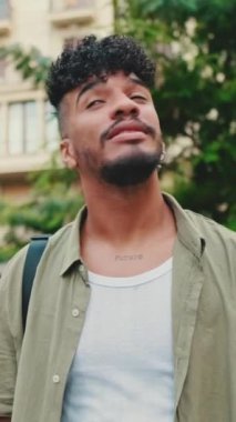 VERTICAL VIDEO: Young happy man with beard dressed in an olive-colored shirt walks along the street of the old city, looks to the side