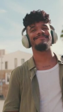 VERTICAL VIDEO: Young man with beard in an olive-colored shirt listens to music on headphones, dances