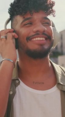 VERTICAL VIDEO: Close up, young man with beard in an olive-colored shirt listens to music on headphones, dances