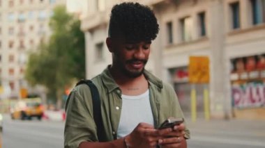 Young happy man with beard dressed in an olive-colored shirt walks through the center of the old city using mobile phone