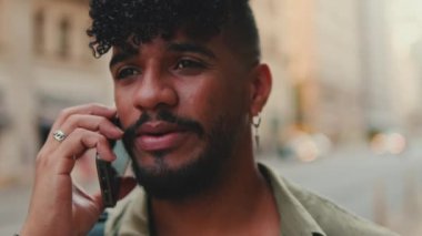 Portrait, close up of young happy man with beard dressed in an olive-colored shirt is talking on cellphone
