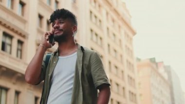 Young happy man with beard dressed in an olive-colored shirt is talking on cellphone standing on the old city background