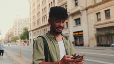 Young happy man with beard dressed in an olive-colored shirt walks through the center of the old city using mobile phone