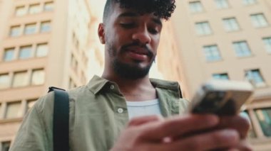 Close up, young man with beard dressed in an olive-colored shirt walks through the center of the old city using mobile phone
