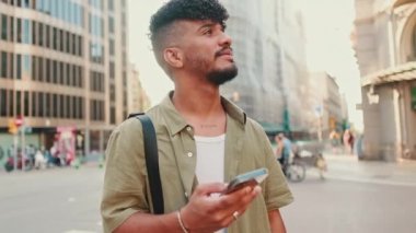 Young smiling man dressed in an olive-colored shirt stands with cellphone in his hand on modern building background