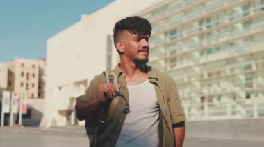 Young male student dressed in an olive colored shirt looking around from outside next to the university