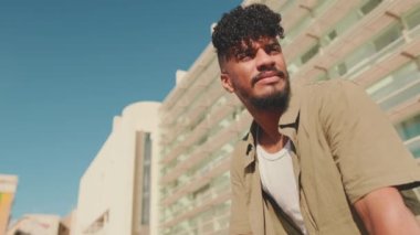 Close up, young male student dressed in an olive colored shirt sits outside next to university