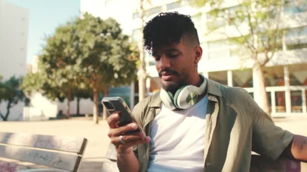 Young Man Beard Wearing Olive Colored Shirt Headphones Sits Bench — Vídeos de Stock