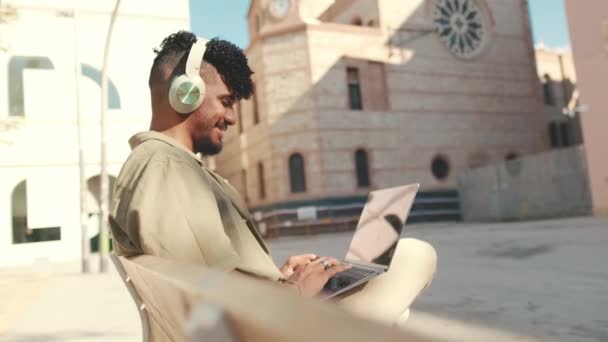 Молодий Студент Чоловічої Статі Навушниках Працює Ноутбуці Сидячи Лавці Межами — стокове відео