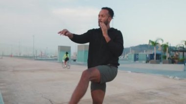 Genç sakallı erkek sporcu, rıhtımda antrenman yaparken elleriyle atlıyor ve hareketler yapıyor.