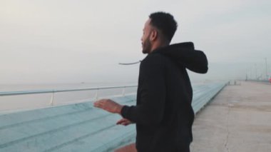 Genç sakallı erkek sporcu, rıhtımda antrenman yaparken elleriyle atlıyor ve hareketler yapıyor.