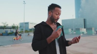 Kapüşonlu giyen genç sakallı erkek sporcu antrenmandan sonra setin üzerinde dururken cep telefonunu kullanıyor.