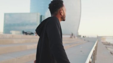 Genç sakallı erkek sporcu setin üzerinde durmuş denize bakıyor.