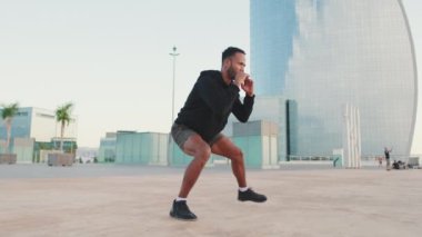 Genç sakallı erkek sporcu idman yapıyor, çömeliyor ve rıhtıma atlıyor.